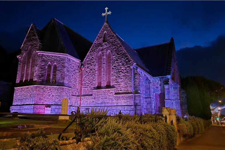 Mere Tapu - the Taranaki Cathedral of St Mary stands illuminated in purple. Te Runanganui 2025 will meet in its hall and at Te Whare Hononga.